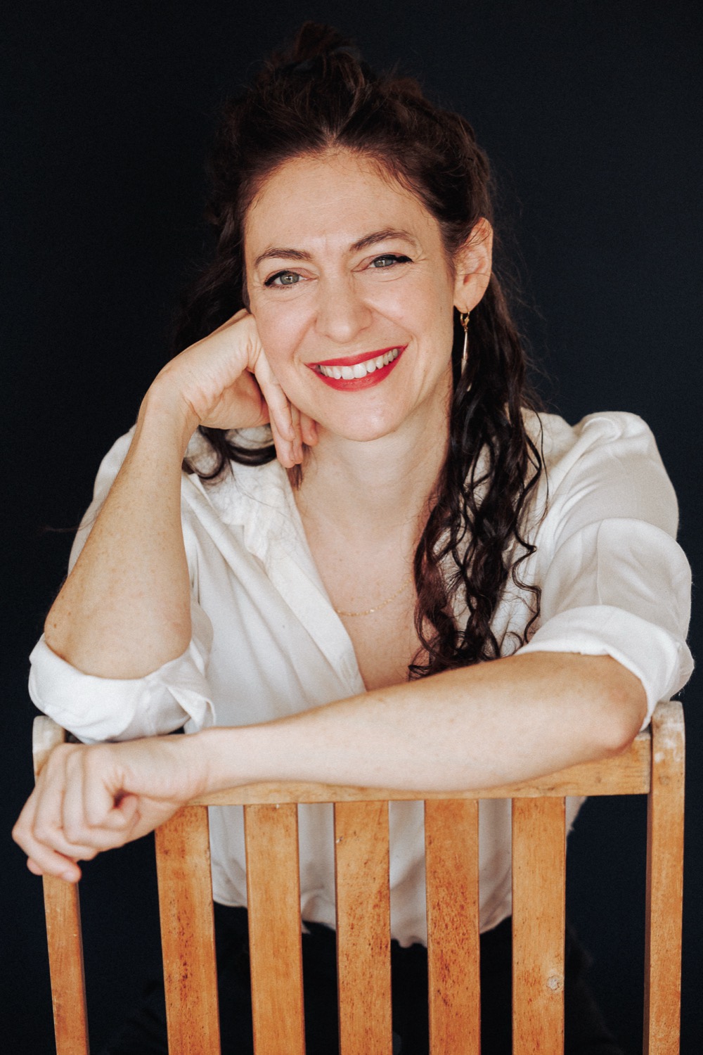 Lucy Antrobus smiling, leaning on the back of a wooden chair