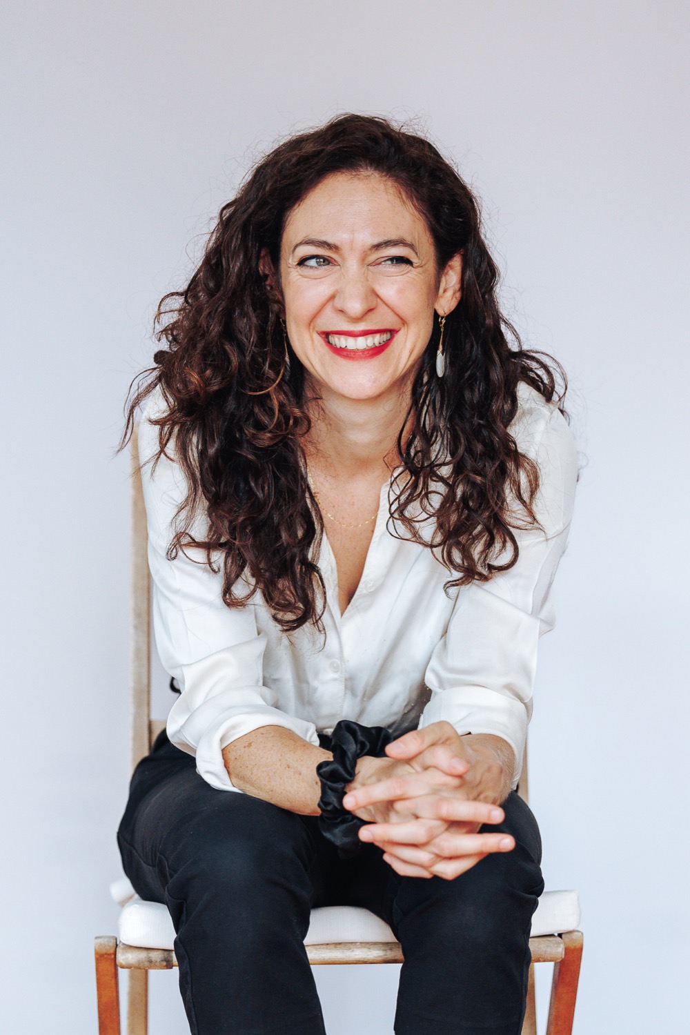 Lucy Antrobus laughing, seated on a chair against a light background