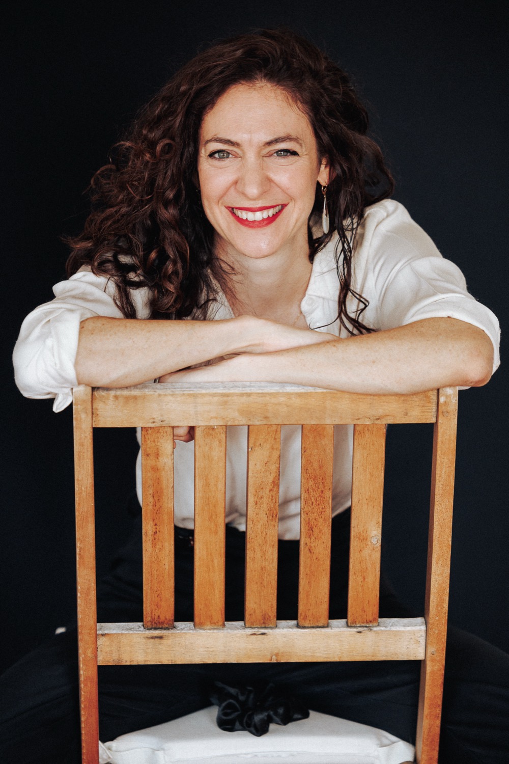 Lucy Antrobus, smiling, arms folded over the back of a wooden chair