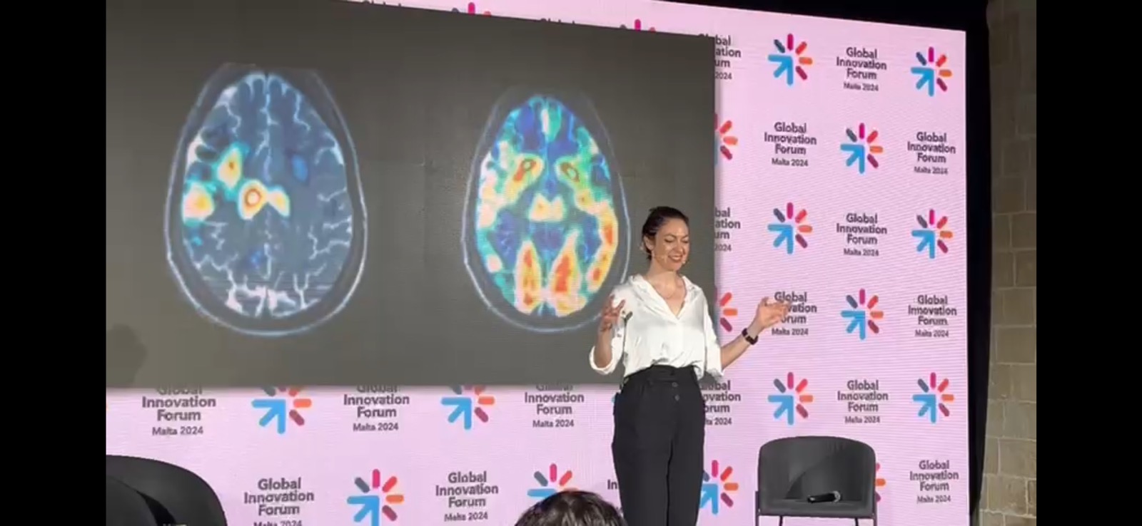 Lucy Antrobus on stage at the Global Innovation Forum with brain scans projected behind her